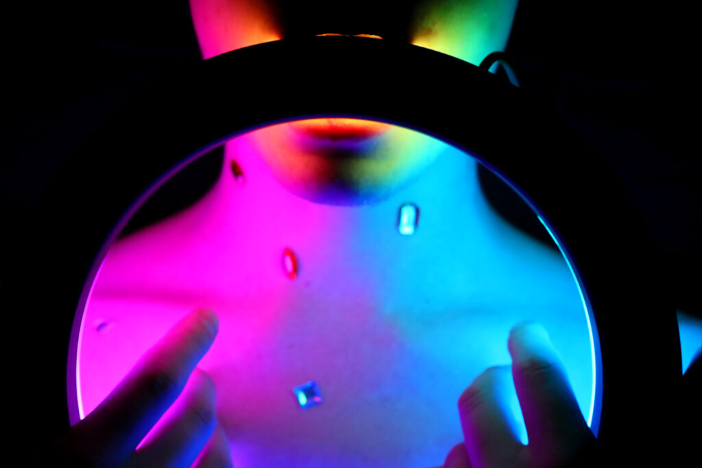 Torse éclairé en rose et bleu vu à travers une loupe, mains au premier plan — photographie de Richard Schlang
