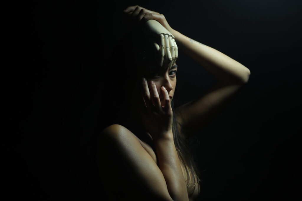 Rosy pose dans l’ombre avec une main articulée en bois sur le front — DETAIL IDENTITY [05], 2019