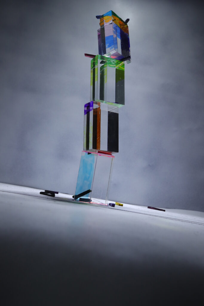 TOTEM ONE : empilement vertical de formes rectangulaires transparentes et colorées sur fond gris.
