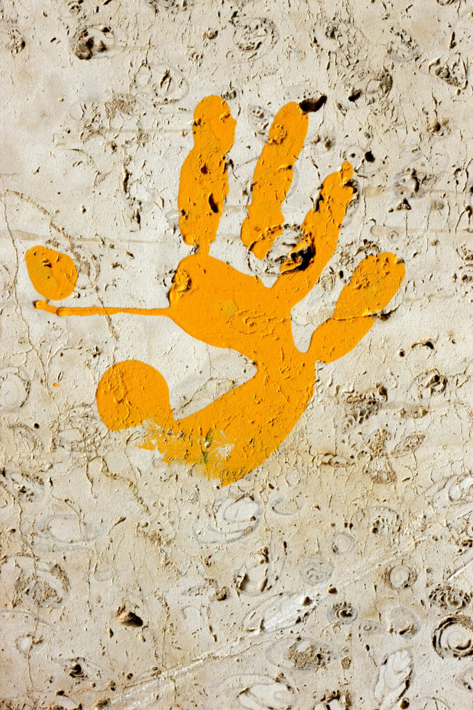 Empreinte de main orange peinte sur un mur blanc à la surface rugueuse — photographie de Richard Schlang