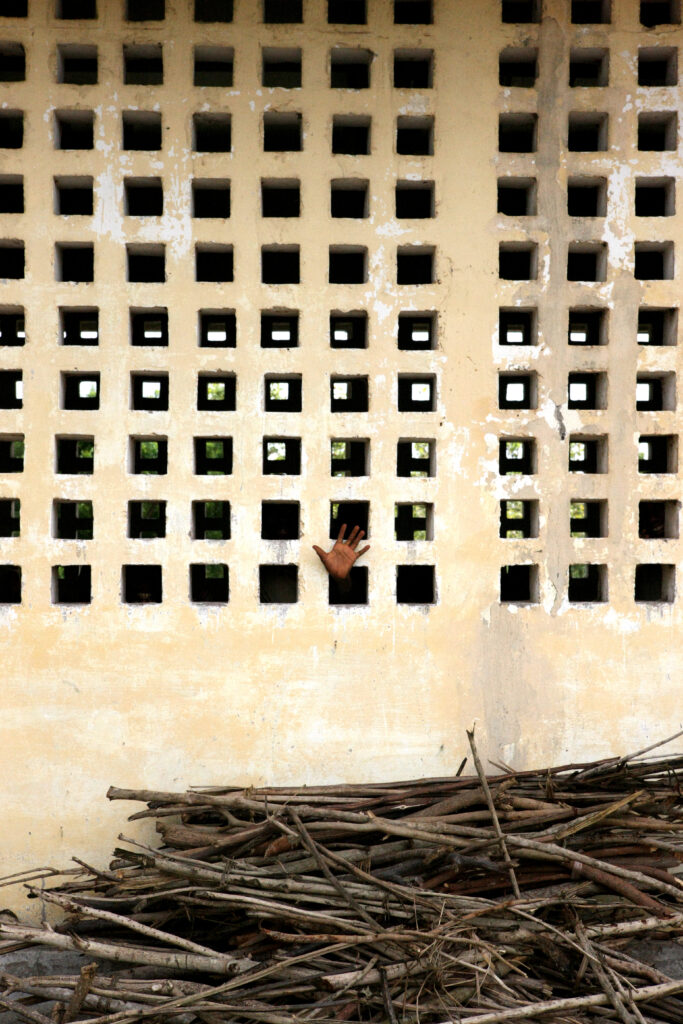 BIENVEILLANCE : une main ouverte apparaît à travers un mur ocre ajouré, au-dessus d’un tas de branches à Lomé.
